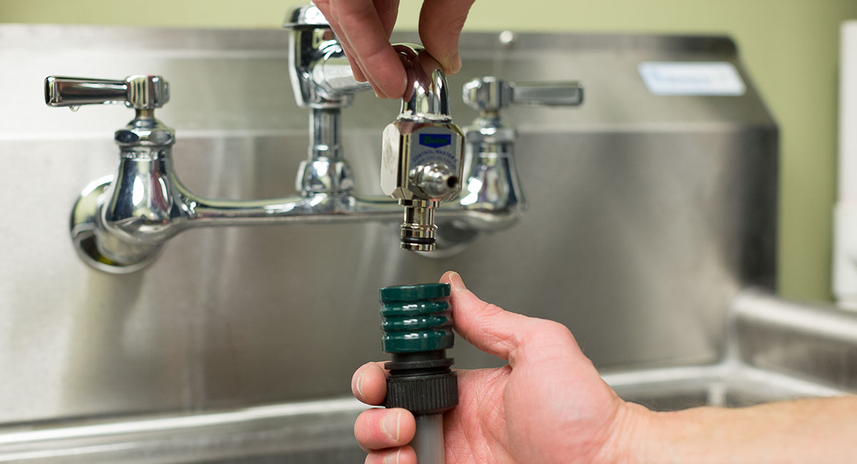 A hand connecting an Action Control System to a faucet.
