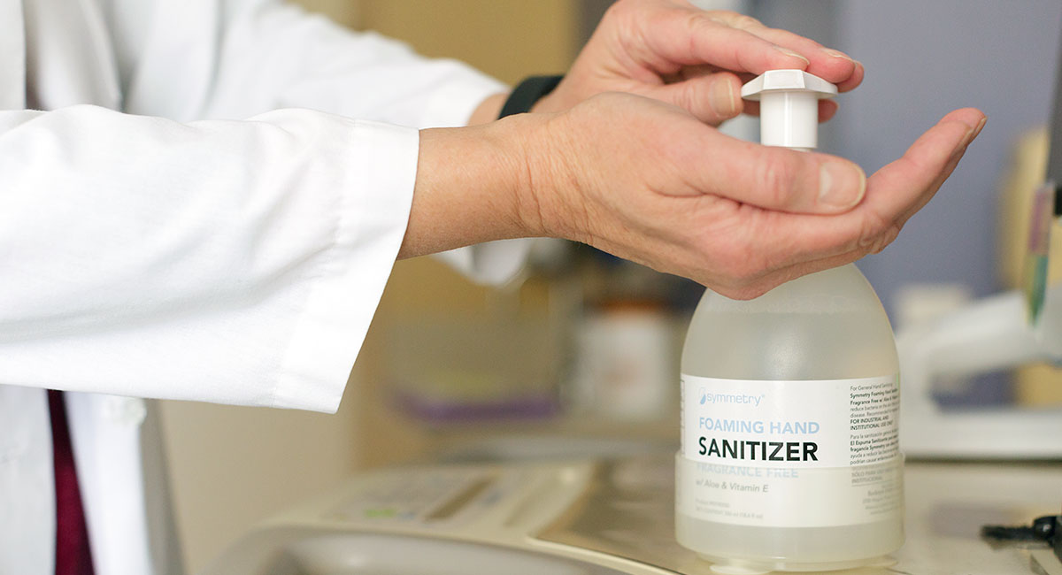 A doctor's hands using 55ml Symmetry Foaming Hand Sanitizer in a suction cup