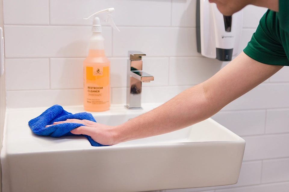 Hand using a microfiber to wipe down sink with Buckeye Eco Pods Restroom Cleaner Spray Bottle