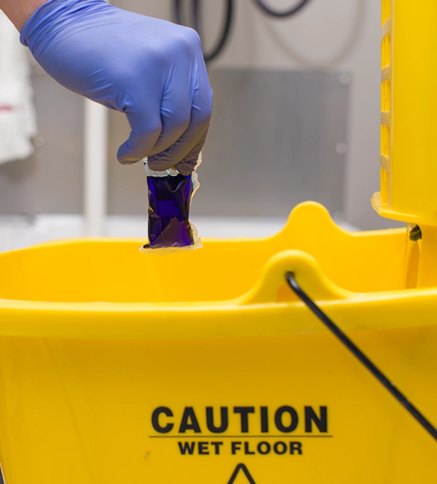 A gloved hand dropping an Eco Pod into a Wet Floor Mop Bucket