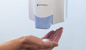 Symmetry dispenser on a wall dispensing Foaming Hand Sanitizer into a hand